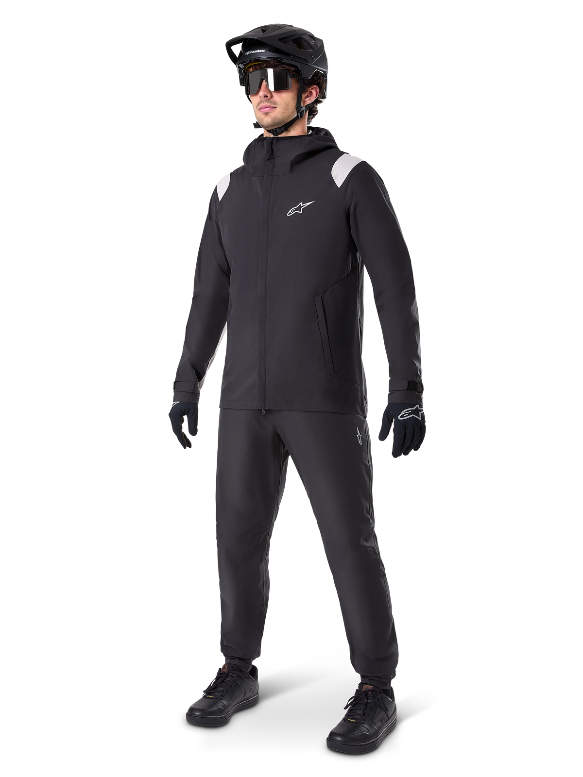 Alpinestars A-Dura regnjacka, svart regnjacka för mountainbike, med vita axeldetaljer, bärs av en cyklist med matchande svart MTB-hjälm, solglasögon, handskar och byxor, teknisk cykeloutfit för alla väder