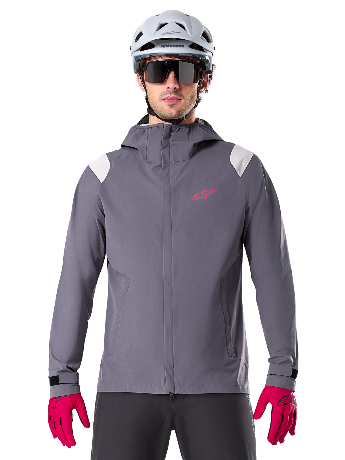 Alpinestars A-Dura regnjacka, MTB-regnjacka, mörk titangrå, design med huva, rosa Alpinestars-logotyp och ljusgrå axelpaneler, bärs med vit MTB-hjälm och starkt rosa handskar, vattentät utrustning för terrängcykling