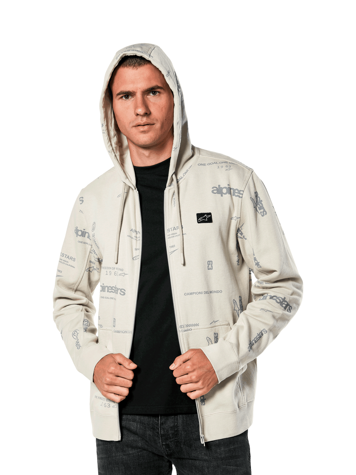 Alpinestars Plenitude Hoodie, vardagliga sportkläder, off-white fleece med dragkedja fram och heltäckande grå logotypsgrafik, bärs av en man med huvan uppe över en svart tröja, med en liten logotyp på bröstet och känguruficka