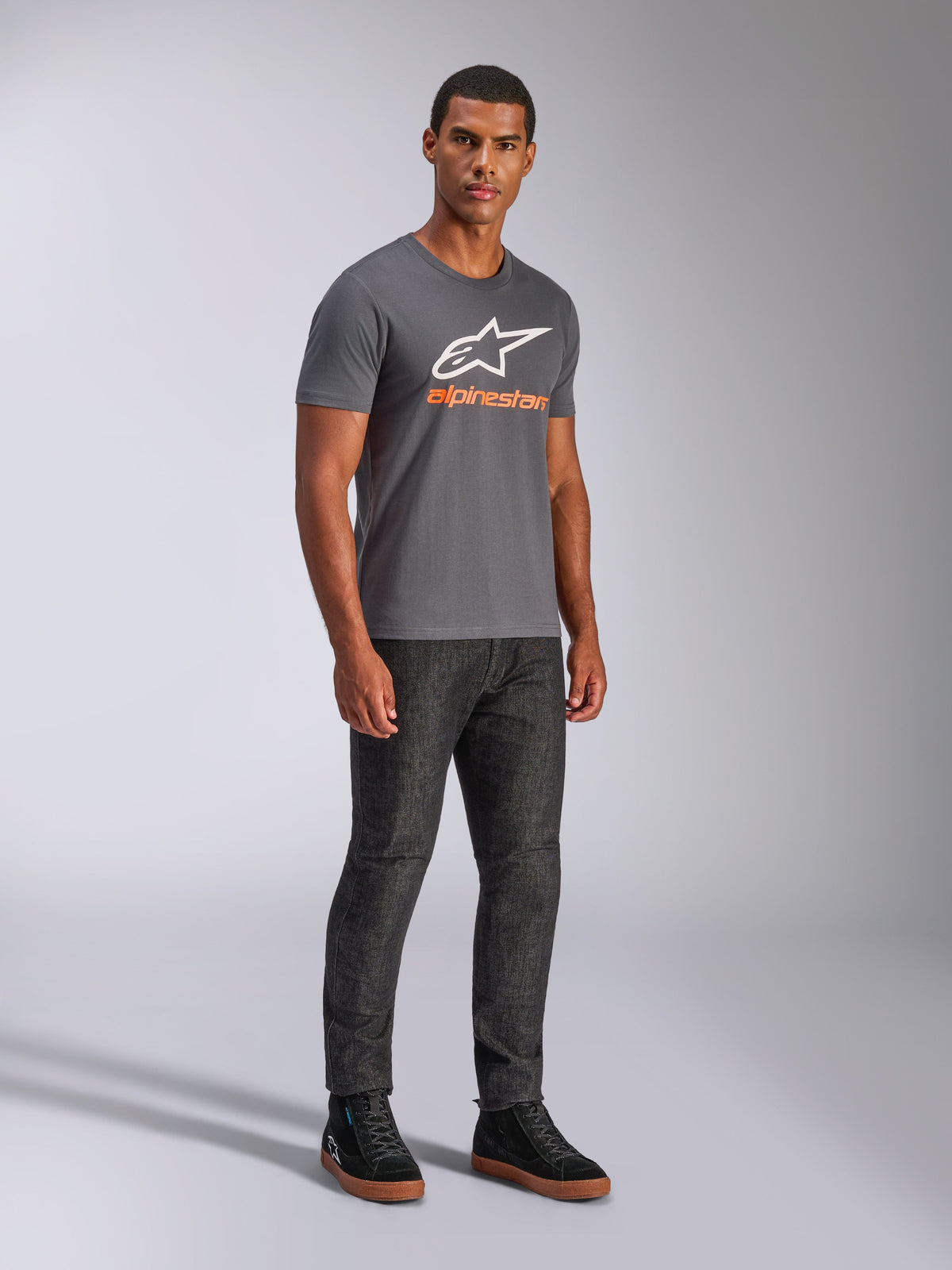 Alpinestars Always 2.0 CSF Tee, kortärmad t-shirt, mörkgrå, vit A-star-logotyp med orange branding, vardaglig motorsport-streetwear buren med mörka jeans och svarta sneakers