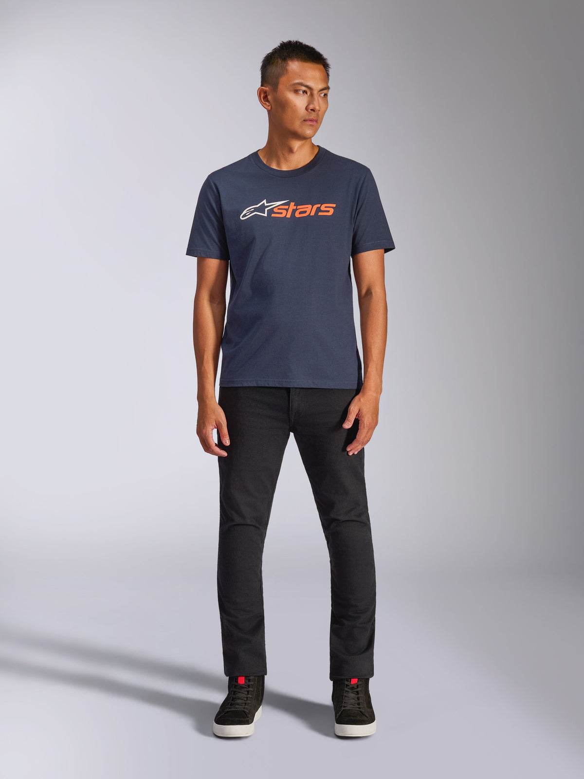 Alpinestars Blaze 2.0 CSF Tee, kortärmad t-shirt, marinblå med vit och orange Astars-logotyp, bärs med svarta byxor och svarta sneakers, avslappnad motorsportinspirerad streetwear