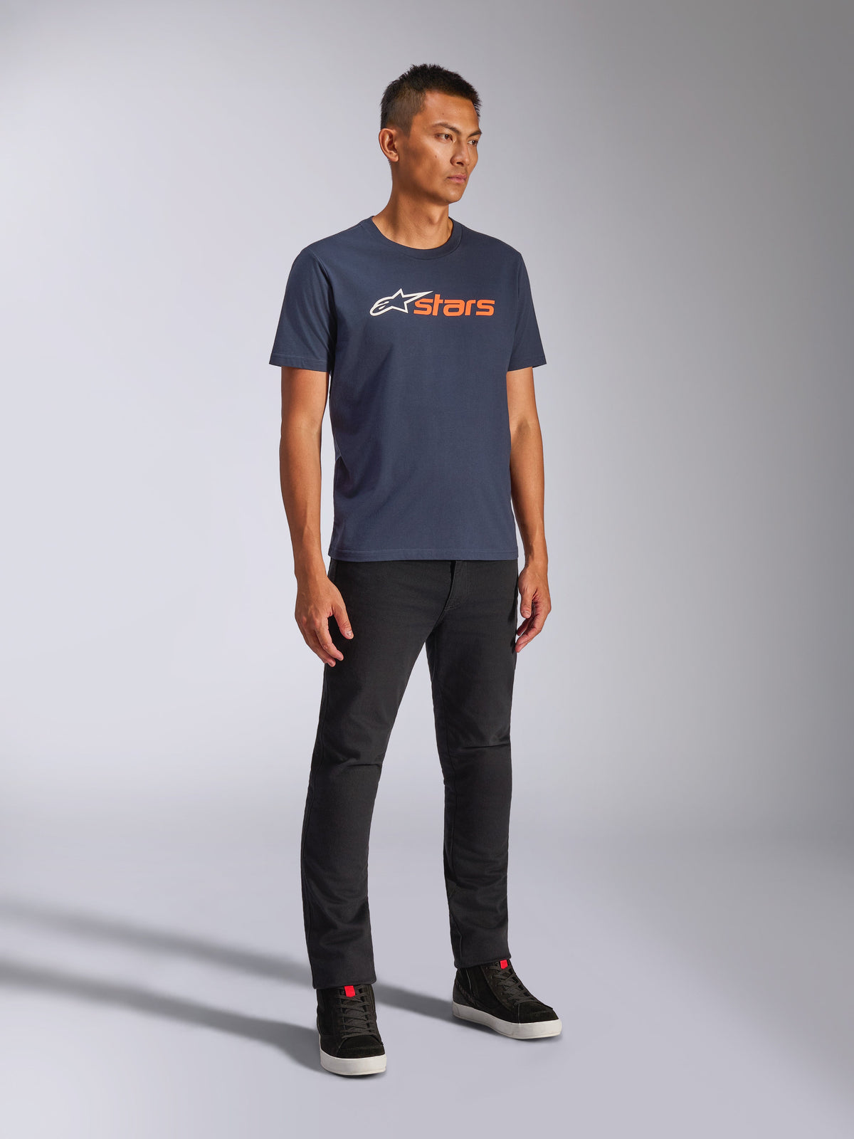Alpinestars Blaze 2.0 CSF T-shirt, kortärmad T-shirt, navyblå med vit och orange Blaze-logotyp, bärs av modell med svarta byxor och sneakers, vardaglig motorsport-inspirerad streetwear