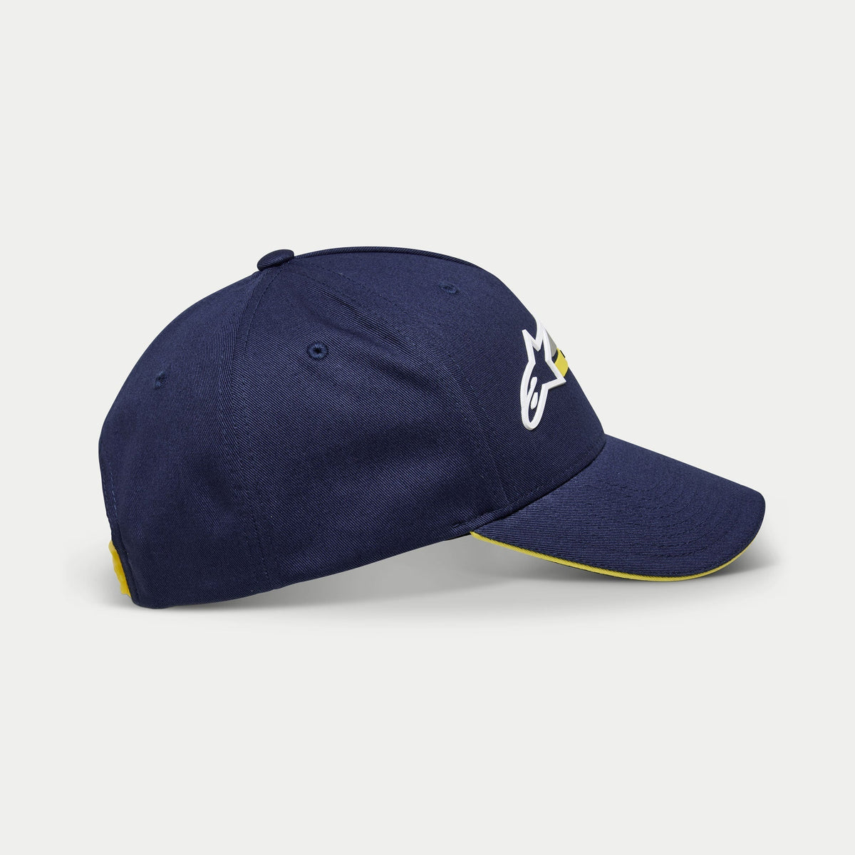 Alpinestars Par keps, marinblå baseballkeps, sidovy som visar vitt och gult logotypbroderi, böjd skärm med gul sandwich-kant, avslappnad strukturerad huvudbonad