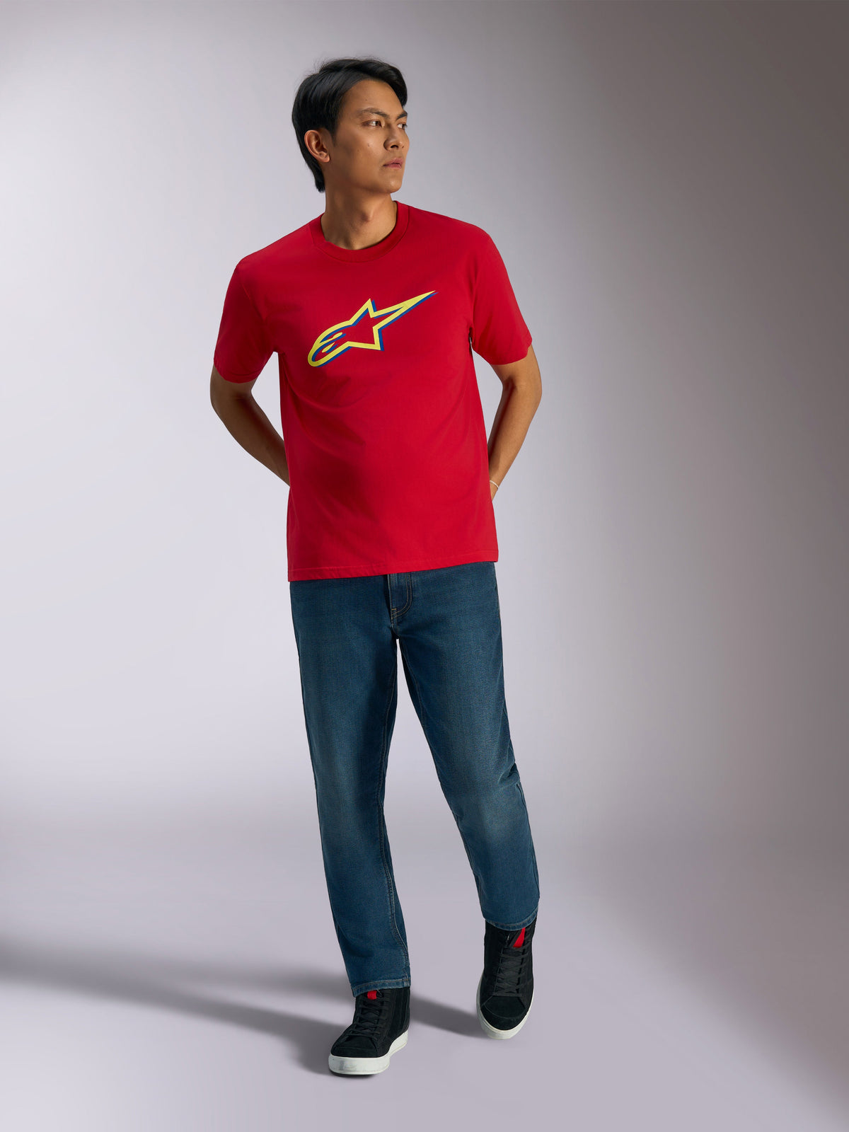 Alpinestars Ageless Shadow CSF Tee, Red Short Sleeve T-Shirt, Yellow and Blue shadow logo graphic, worn with blue jeans and black sneakers, casual motorsport lifestyle apparel