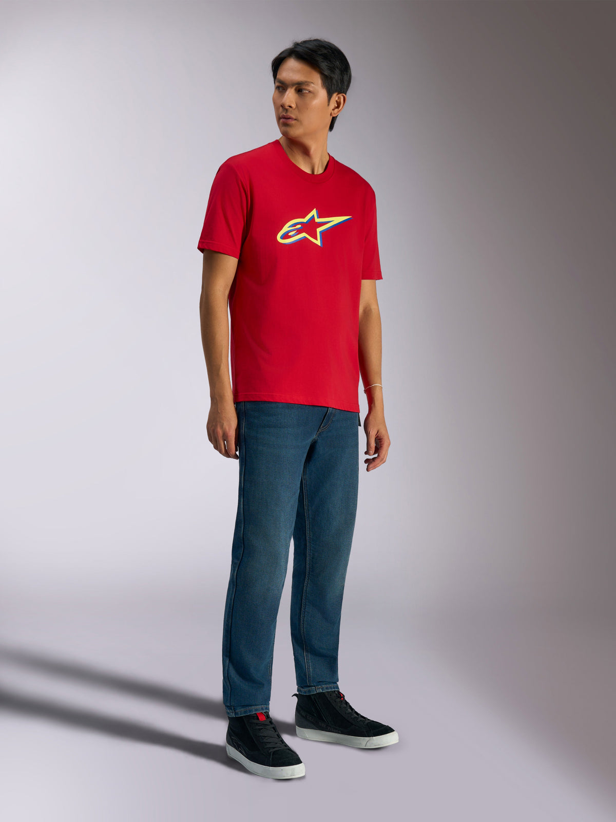 Alpinestars Ageless Shadow CSF Tee, Short Sleeve T-Shirt, Red, featuring Ageless shadow logo with yellow and blue accents, worn by model with denim jeans and black sneakers, Casual Motorsport Streetwear