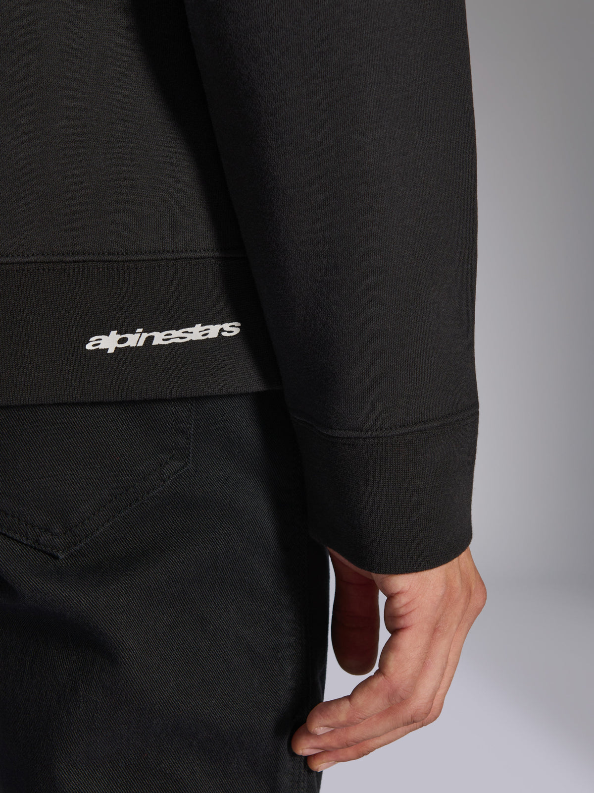 Alpinestars Positive Crew, svart sweatshirt, närbild på ribbad fåll och ärmmudd med vit Alpinestars-logotyp, förstklassig tygstruktur, avslappnade motorsportinspirerade sportkläder