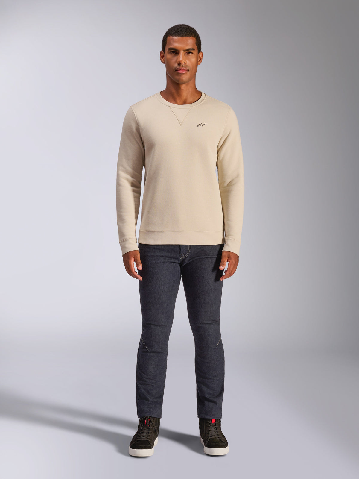 Alpinestars Positive Crew, off-white sweatshirt med rund hals, liten svart logotyp på bröstet, ribbade muddar och fåll, triangelsöm vid halsen, avslappnad motorsport-streetwear som bärs med mörka jeans