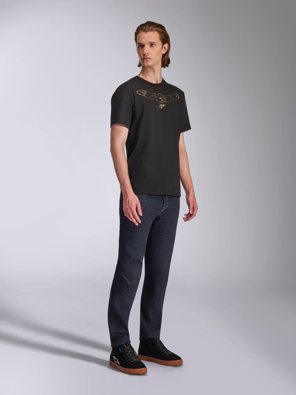 Alpinestars Luxo CSF Tee, kortärmad t-shirt, svart, guldfärgad Astars-logotyp med konturer på bröstet, bärs av modell med mörka jeans och svarta sneakers, casual motorsport-streetwear