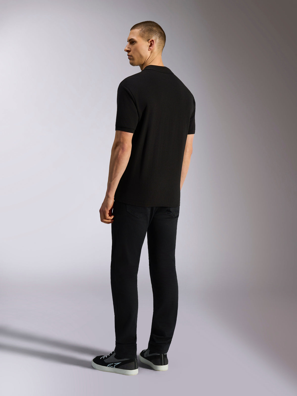 Alpinestars Endeavor Classic Polo, Short Sleeve Pique Polo Shirt, Black, back view of male model wearing black pants and sneakers, casual motorsport-inspired streetwear
