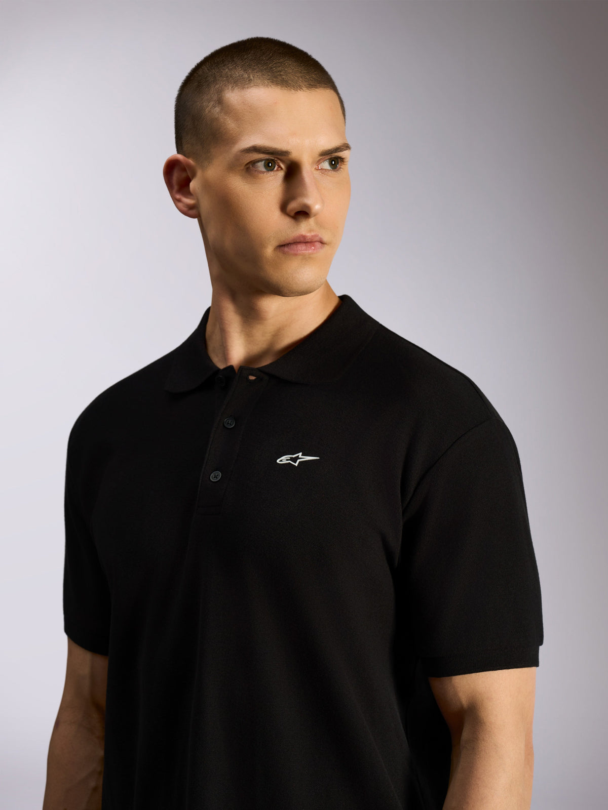 Alpinestars Endeavor Classic Polo, Black pique polo shirt worn by a male model, small white Astars logo on chest, three-button placket and ribbed collar, casual motorsport streetwear