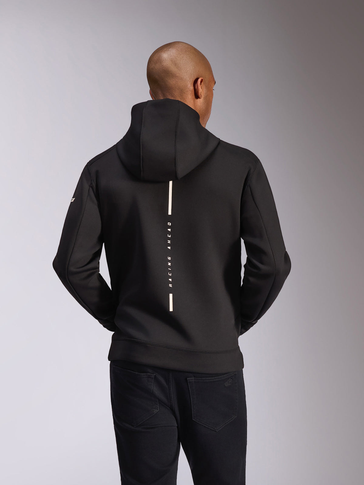 Alpinestars Insight huvtröja, sedd bakifrån, svart, vertikal vit rand med texten "RACING AHEAD", logotyp på ärmen, avslappnat motorsport-inspirerat streetwear