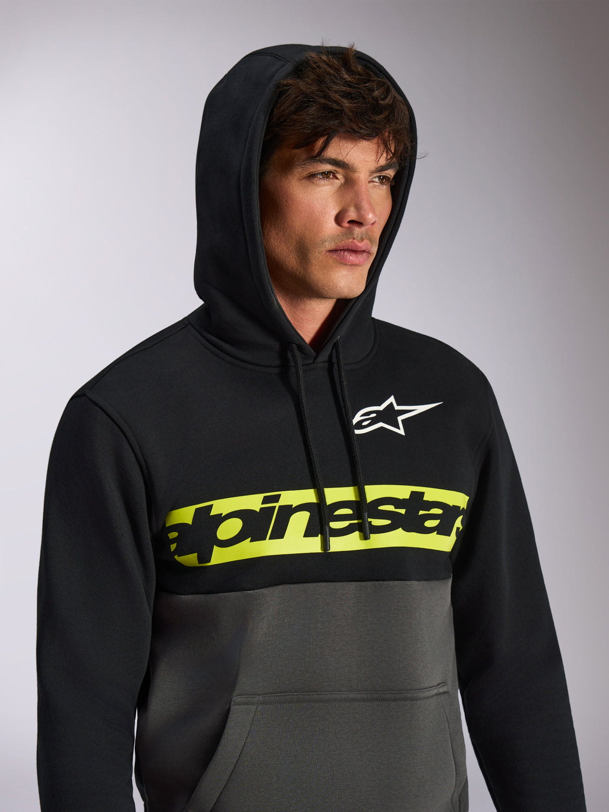 Alpinestars Parallel Hoodie, avslappnad färgblockerad streetwear, svart överdel och mörkgrå (gunmetal) nederdel, neongult bröstband med svart Alpinestars ordlogotyp, vit Astars-logotyp, huvtröja med dragsko