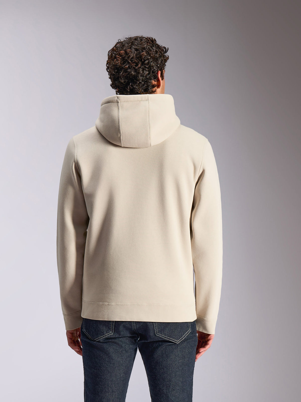 Alpinestars Pulse Hoodie, sandfärgad, baksida av manlig modell som bär den enfärgade huvtröjan, kombinerad med mörka denimjeans, avslappnad motorsportinspirerad streetwear