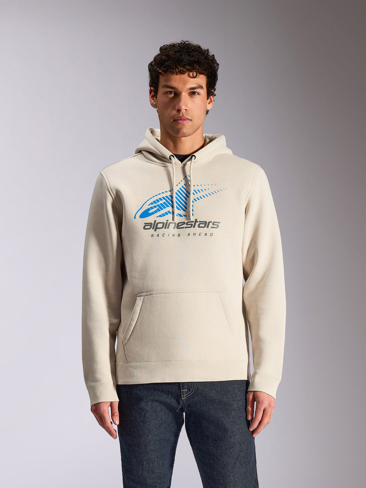 Alpinestars Pulse Hoodie, off-white avslappnad huvtröja, blå och grå Astars Combo-logotyp framtill med speed line fade-grafik, känguruficka fram, bärs av modell med mörka jeans, motorsport-inspirerad streetwear