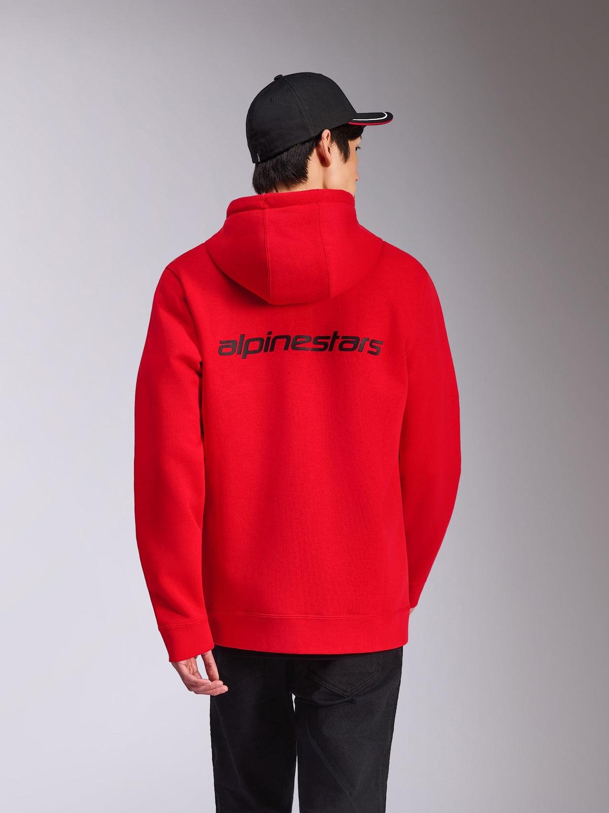 Alpinestars Transverse Hoodie, röd, vy bakifrån med svart Alpinestars-ordlogotyp över ryggen, avslappnad streetwear, huvtröja i fleece med ribbade muddar och fåll, stylad med en svart keps