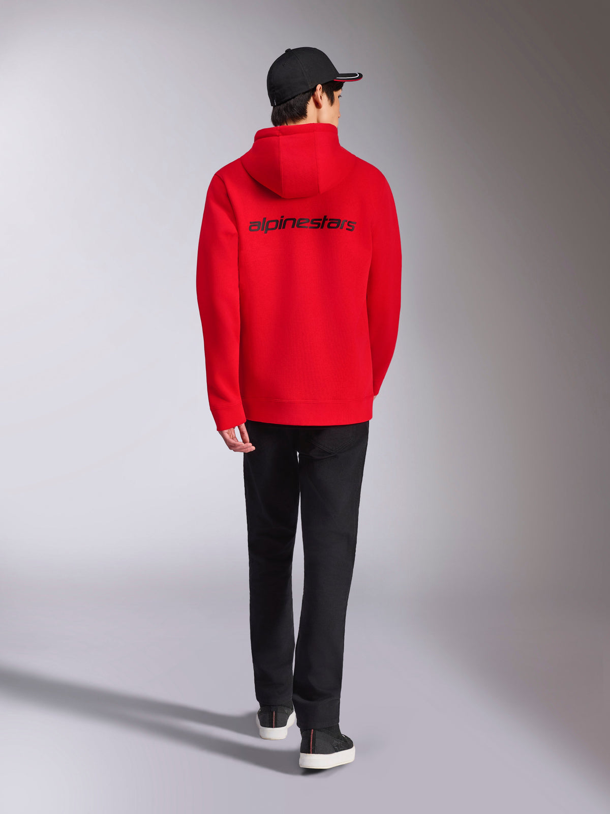 Alpinestars Transverse Hoodie, röd streetwear, vy bakifrån med svart Alpinestars ordlogotyp, huvtröja i fleece, stylad med svart keps och svarta byxor