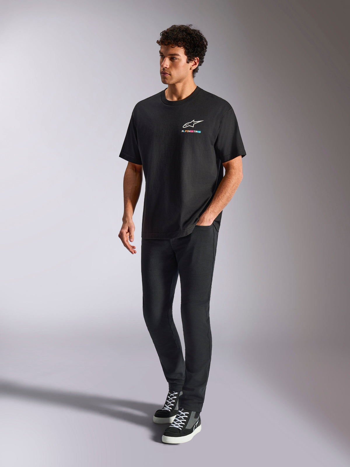 Alpinestars Wild Oversized CSF Tee, kortärmad t-shirt, svart, flerfärgad Astars-logotyp på bröstet, avslappnad streetwear-stil bärs av en modell med svarta byxor och high-top sneakers