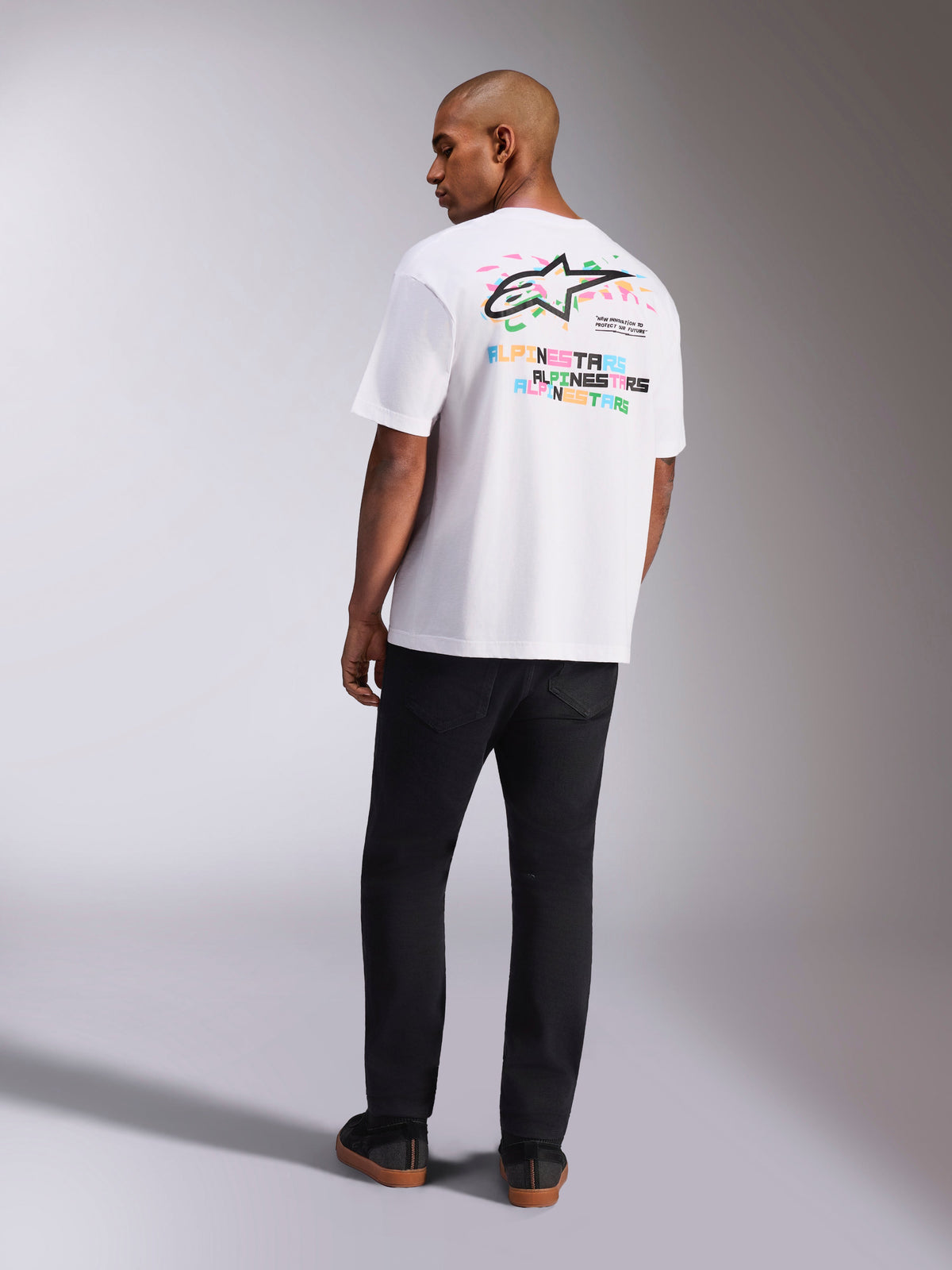Alpinestars Wild Oversized CSF Tee, kortärmad t-shirt, vit, vy bakifrån av modell som bär en oversized t-shirt med livfull flerfärgad Astars-logotyp och staplad text på ryggen, avslappnad motorsport-inspirerad streetwear