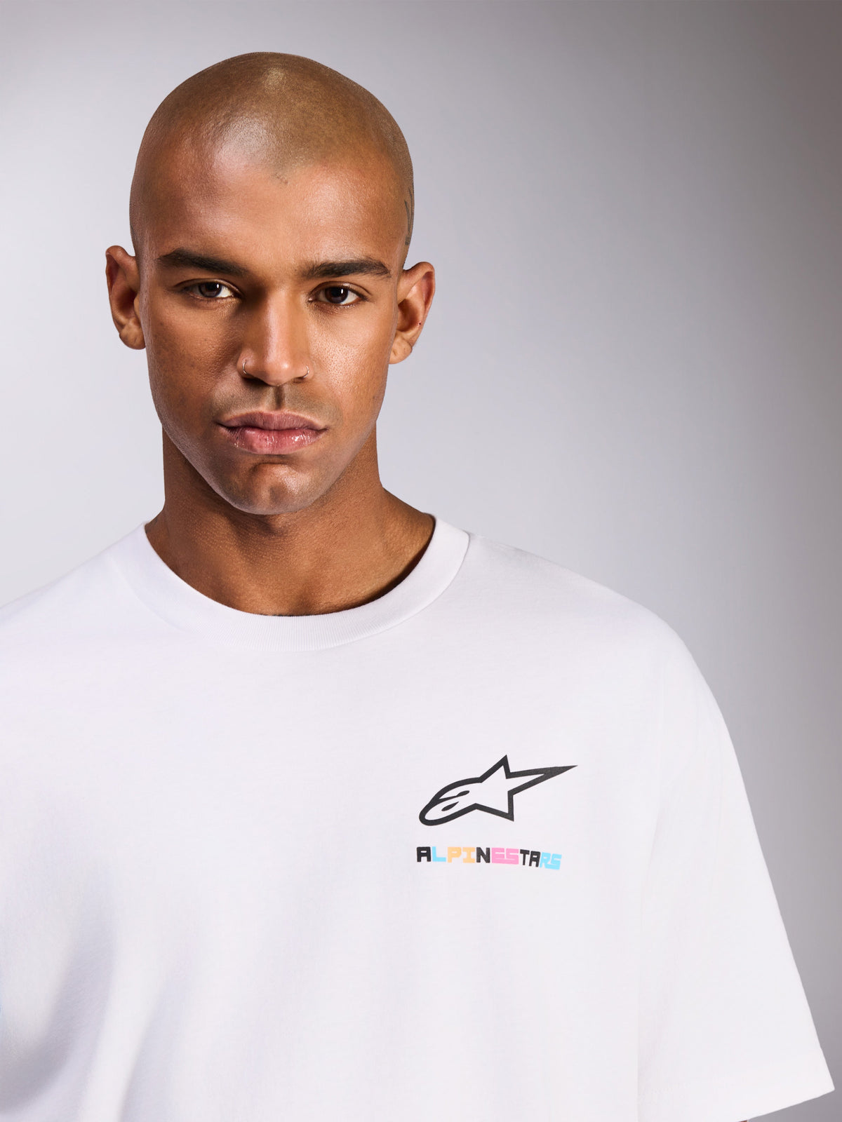 Alpinestars Wild Oversized CSF Tee, vit kortärmad t-shirt på manlig modell, svart Astars-logotyp med livfull flerfärgad text på bröstet, casual streetwear-stil