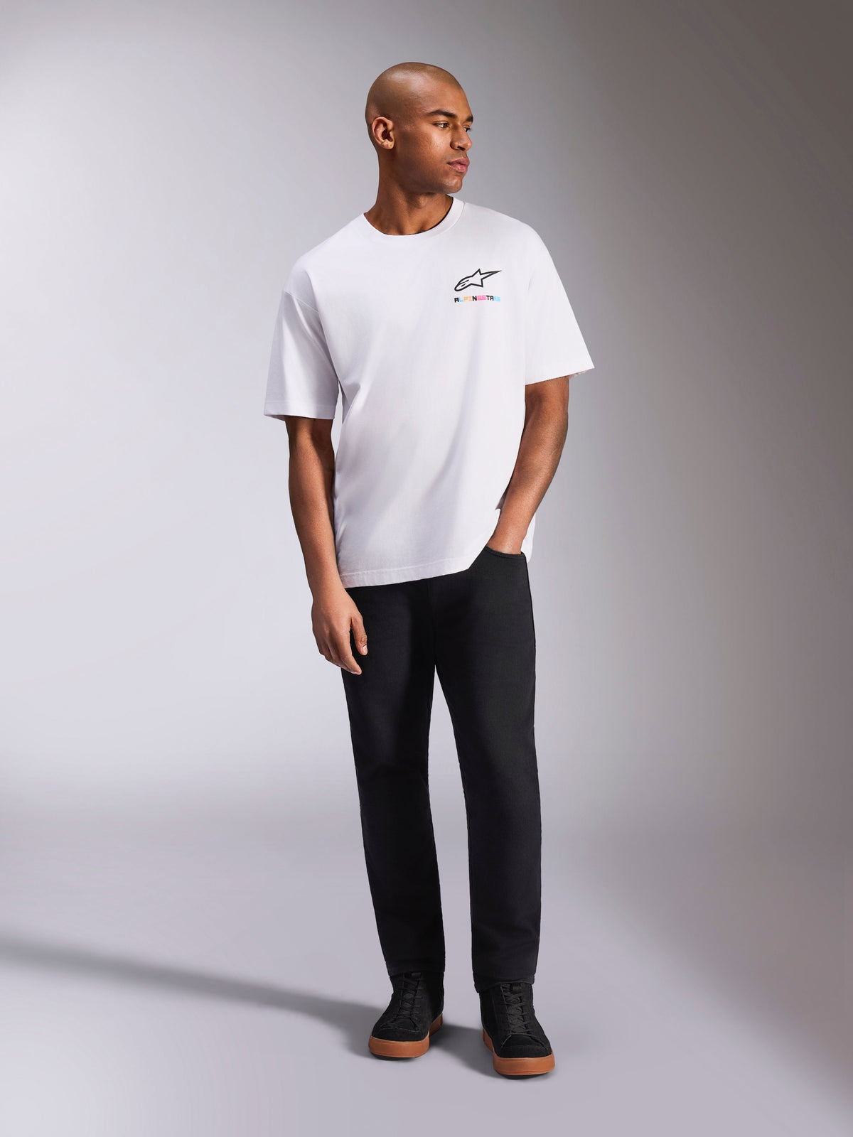 Alpinestars Wild Oversized CSF Tee, kortärmad t-shirt, vit, livfull flerfärgad Astars-logotyp på bröstet, bärs med svarta byxor och sneakers, avslappnade motorsport-livsstilskläder