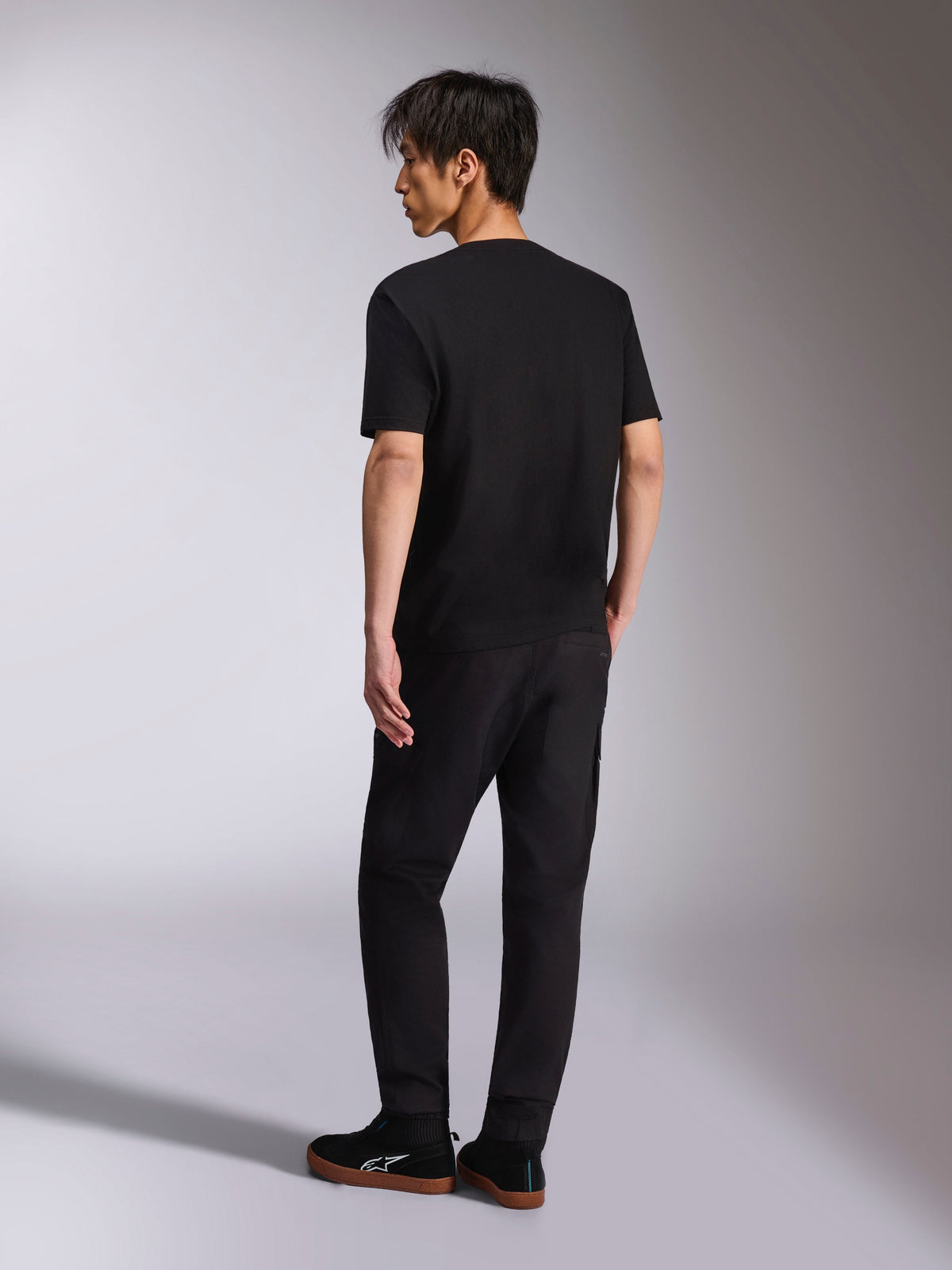 Alpinestars Noka CSF Tee, kortärmad t-shirt, svart, baksida visas på modell, kombinerad med svarta byxor och vardagliga sneakers, minimalistisk motorsport-streetwear