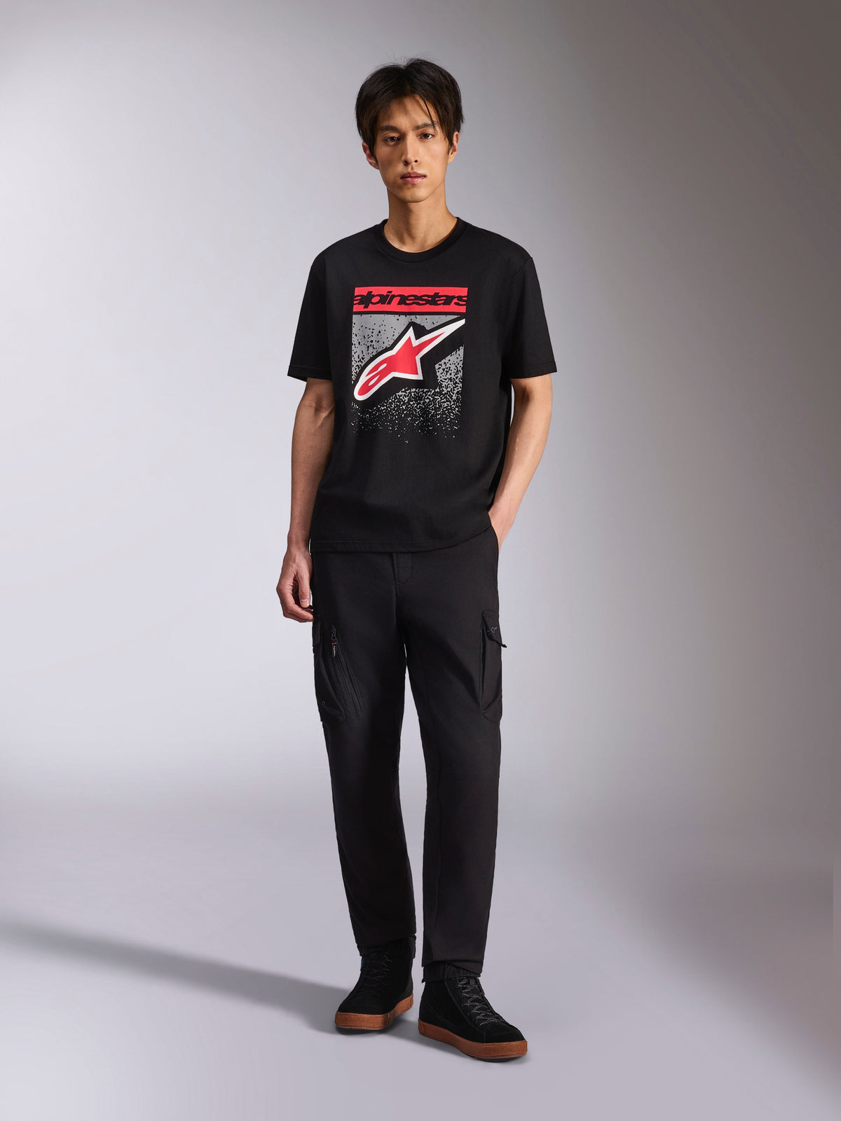 Alpinestars Noka CSF Tee, kortärmad t-shirt, svart, Astars-logotyp på framsidan med röd och vit MX-övertoningsgrafik, bärs av en modell med svarta cargobyxor, casual motorsport-streetwear