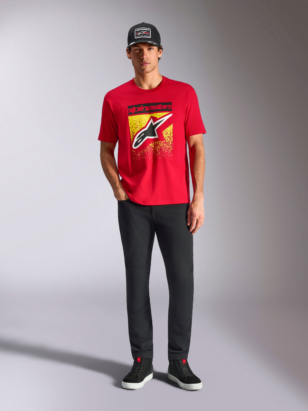 Alpinestars Noka CSF Tee, kortärmad t-shirt, röd, med en stor Astars-logotyp framtill med gul och svart MX-gradering, bärs med svarta byxor och en svart keps, casual motorsport-streetwear