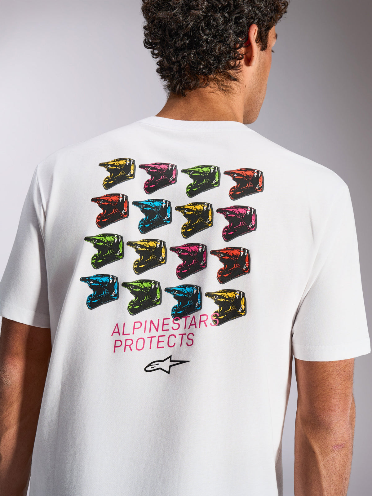 Alpinestars Pop Helmet CSF Tee, kortärmad t-shirt, vit, grafik på baksidan med ett rutmönster av färgglada M10-hjälmar, texten 'ALPINESTARS PROTECTS' och Astars-logotyp, avslappnade motorsportkläder