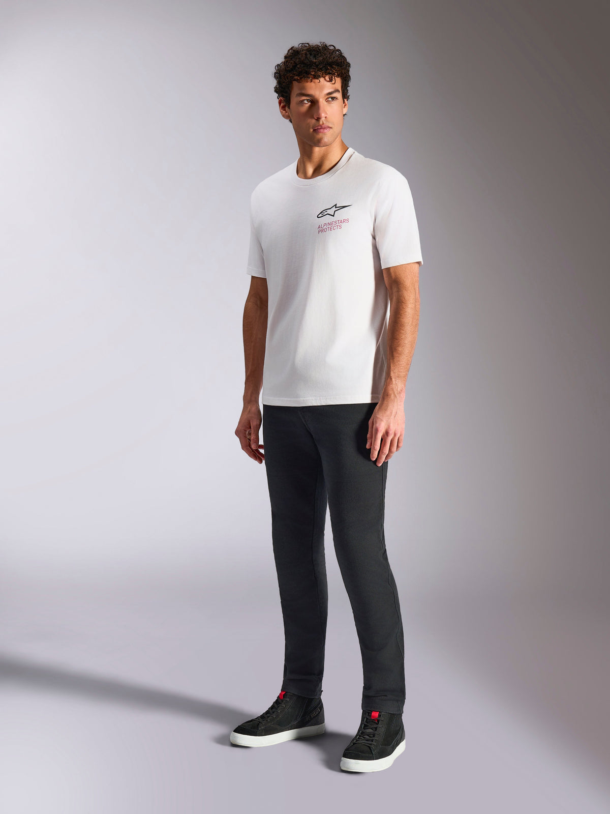 Alpinestars Pop Helmet CSF Tee, kortärmad t-shirt, vit, med Astars-logotyp på framsidan och röd text, bärs av en manlig modell med mörka byxor och svarta sneakers, casual motorsport streetwear