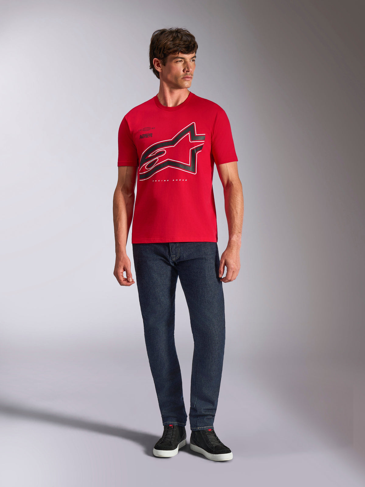 Alpinestars Authority CSF Tee, kortärmad t-shirt, röd, stor svart beskuren Astars-logotyp med vit kontur, bärs med mörkblå jeans och svarta sneakers, vardagligt motorsportinspirerat streetwear