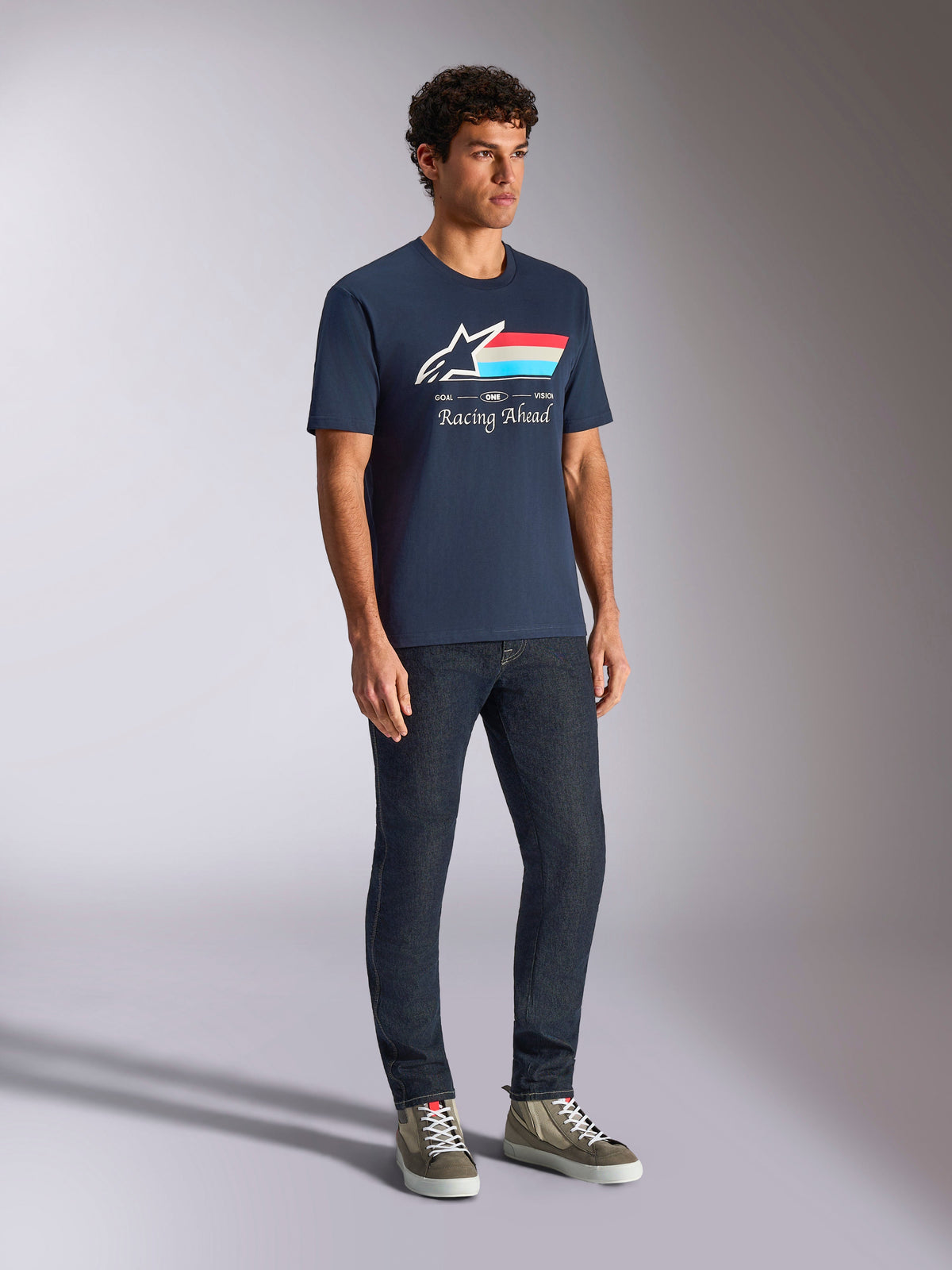 Alpinestars Trifecta CSF Tee, kortärmad t-shirt, marinblå, med Astars-logotyp, trefärgade ränder och Racing Ahead-text, bärs av en modell med mörka jeans och sneakers, avslappnad motorsport-inspirerad streetwear