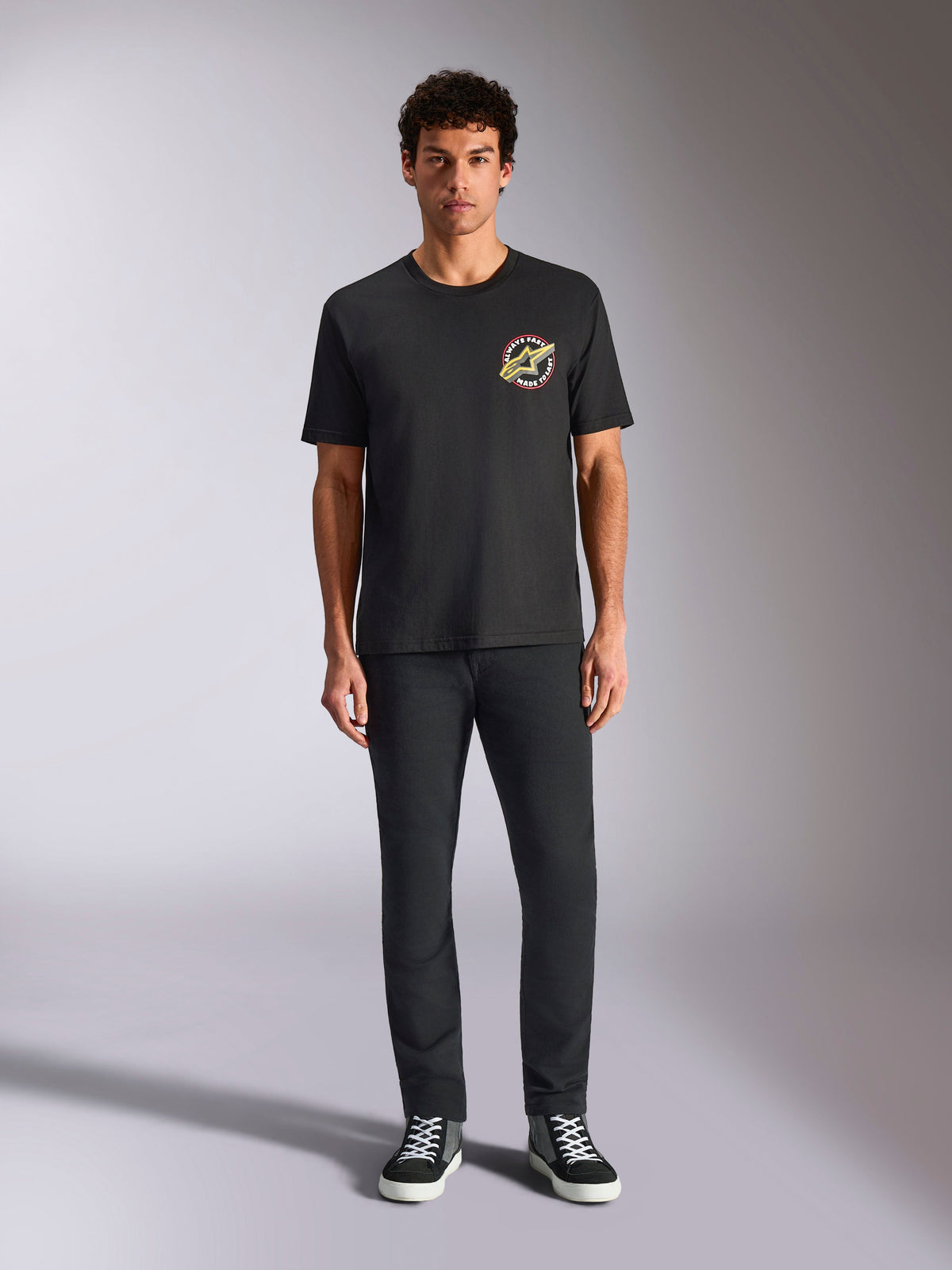 Alpinestars Aorbit CSF Tee, kortärmad t-shirt, svart, cirkulär logotyp med texten 'Always Fast Made to Last' på bröstet, bärs av en modell med svarta byxor och sneakers, avslappnad motorsportinspirerad streetwear