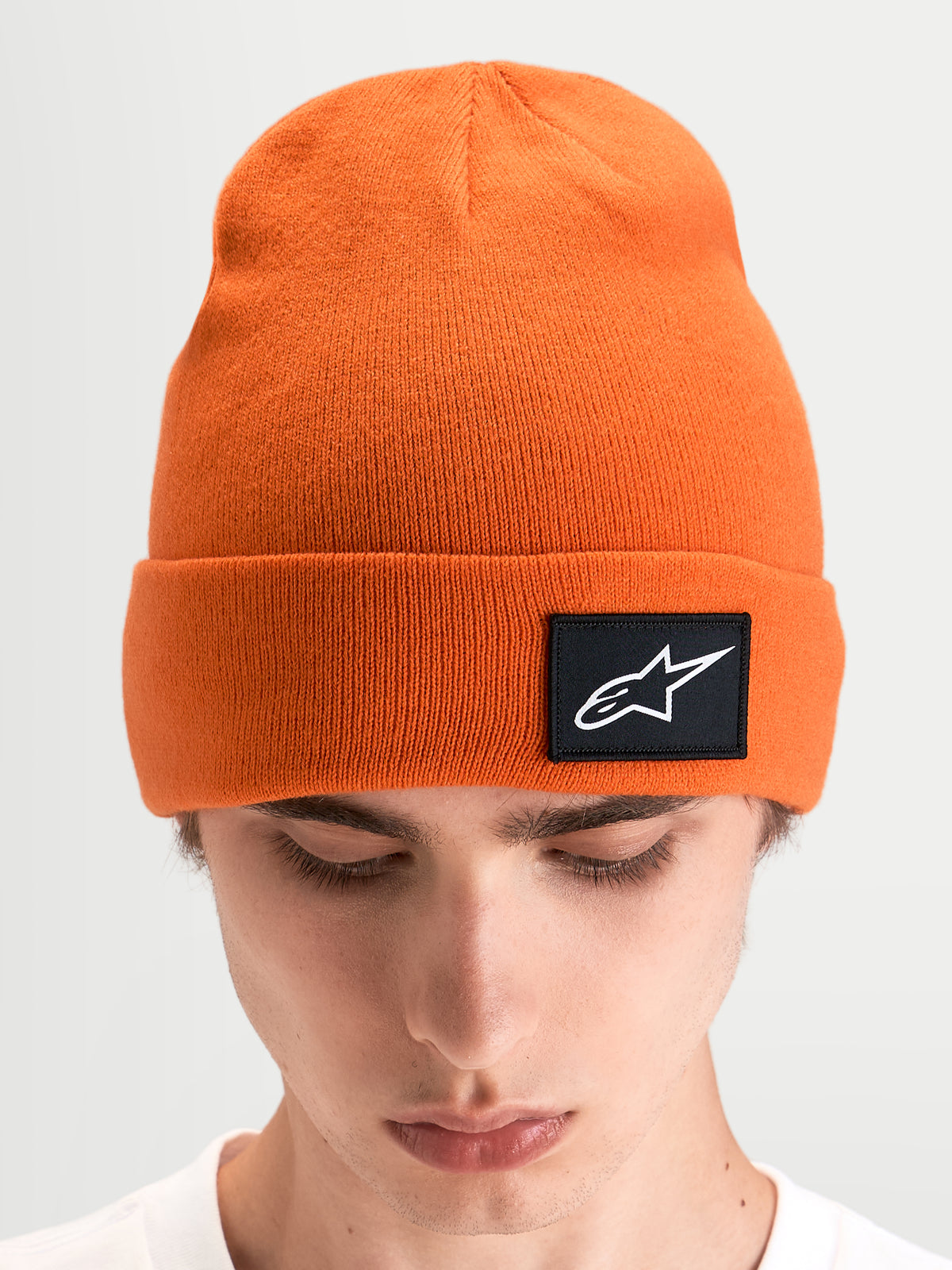 Alpinestars Augment Cuff mössa, orange sportmössa i stickad jerseystruktur med djup passform och svart vävd Astars-logopatch på uppvikta kanten, bärs av en modell