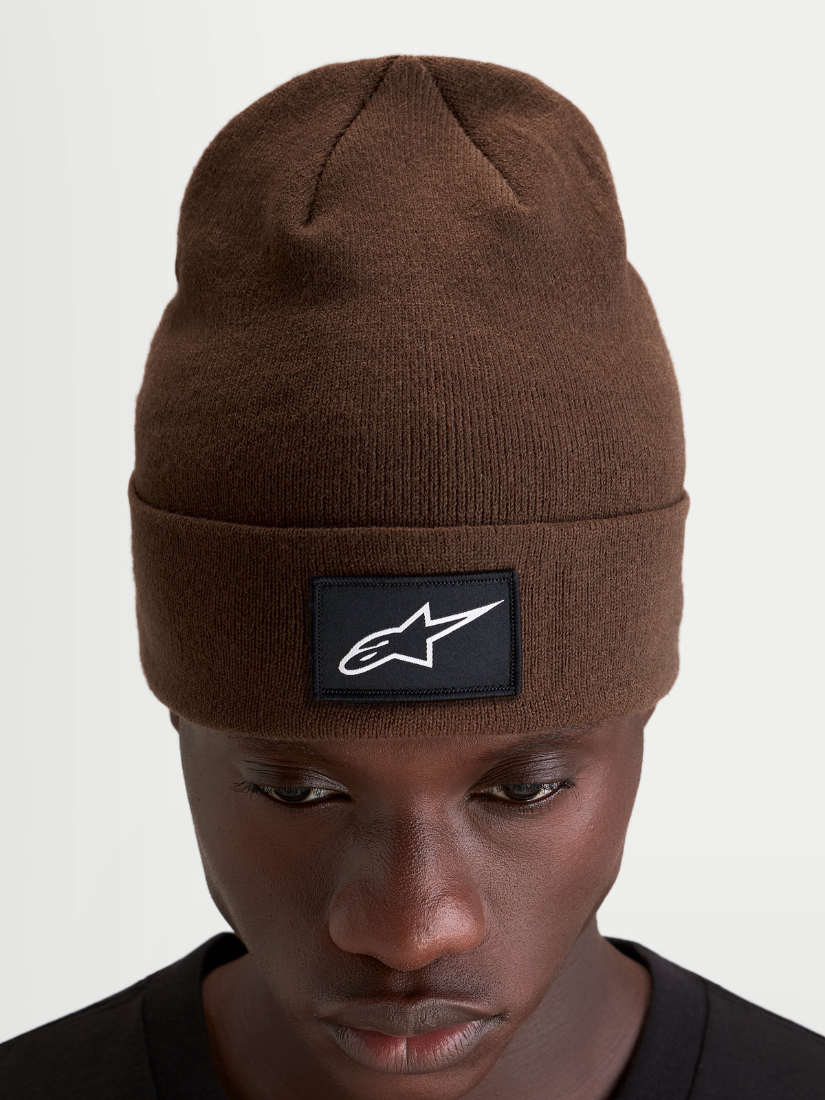 Alpinestars Augment Cuff mössa, brun stickad mössa med en vävd svart-vit Astars-logopatch och djup passform, bärs av en modell