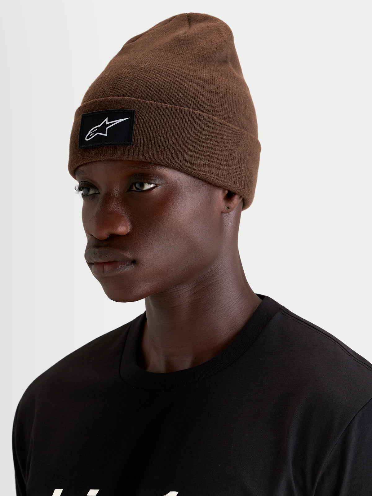 Alpinestars Augment Cuff mössa, brun sportmössa med svartvit vävd logopatch på uppvikbar kant, bars av en modell