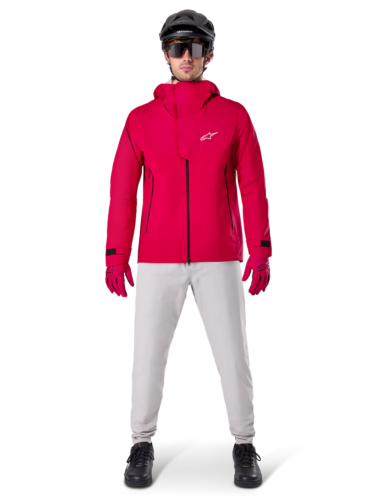 Alpinestars A-Dura Elite vattentät jacka, röd fluo, teknisk mountainbikejacka som bärs med en svart MTB-hjälm, solglasögon, matchande röda handskar och ljusgrå byxor, helkroppsvy av cykelutrustning för alla väder
