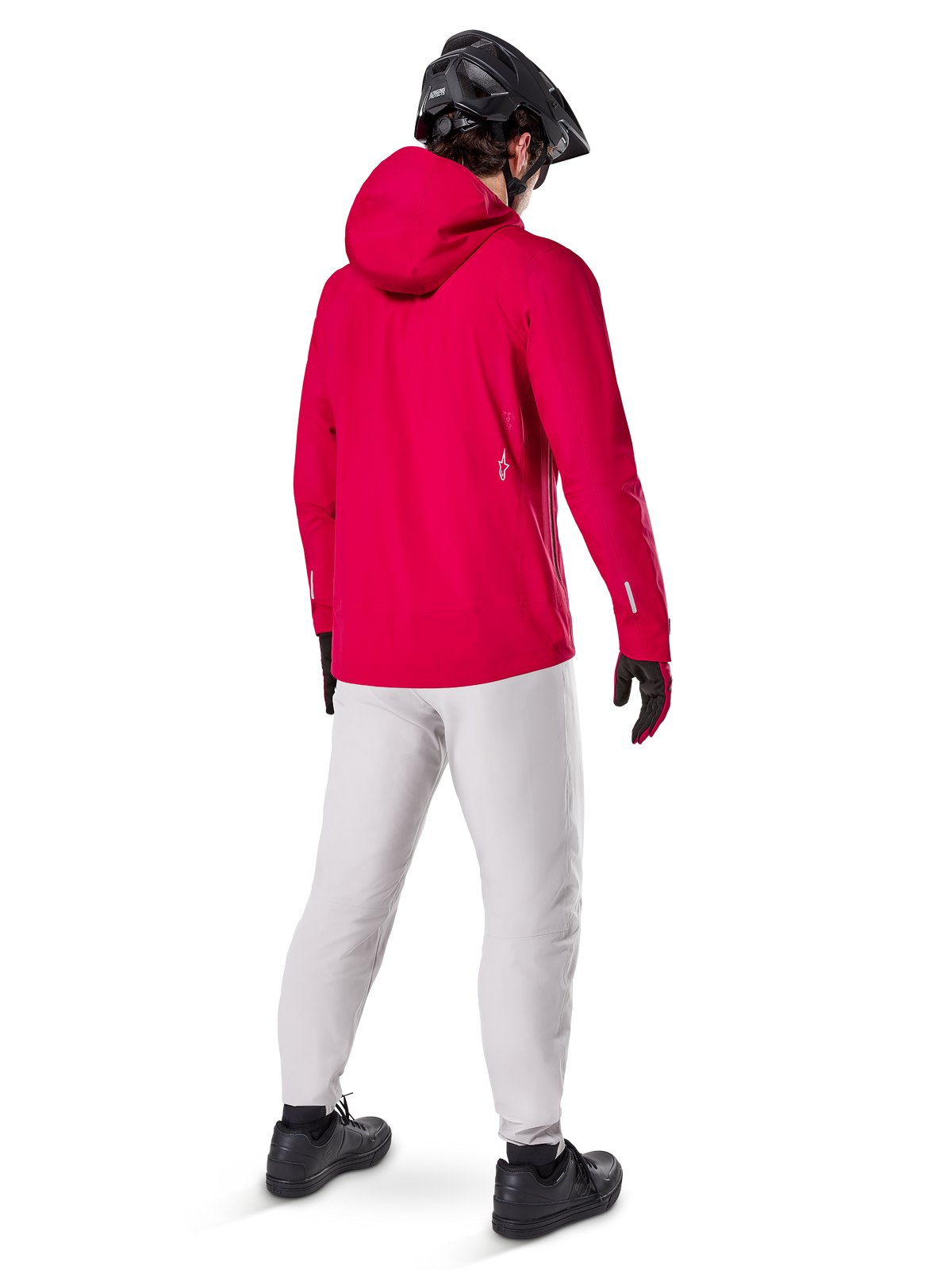 Alpinestars A-Dura Elite vattentät jacka, Red Fluo, sedd snett bakifrån, buren med ljusgrå byxor och svart MTB-hjälm, har huva och reflekterande detaljer, högpresterande cykelregnjacka för stigcykling