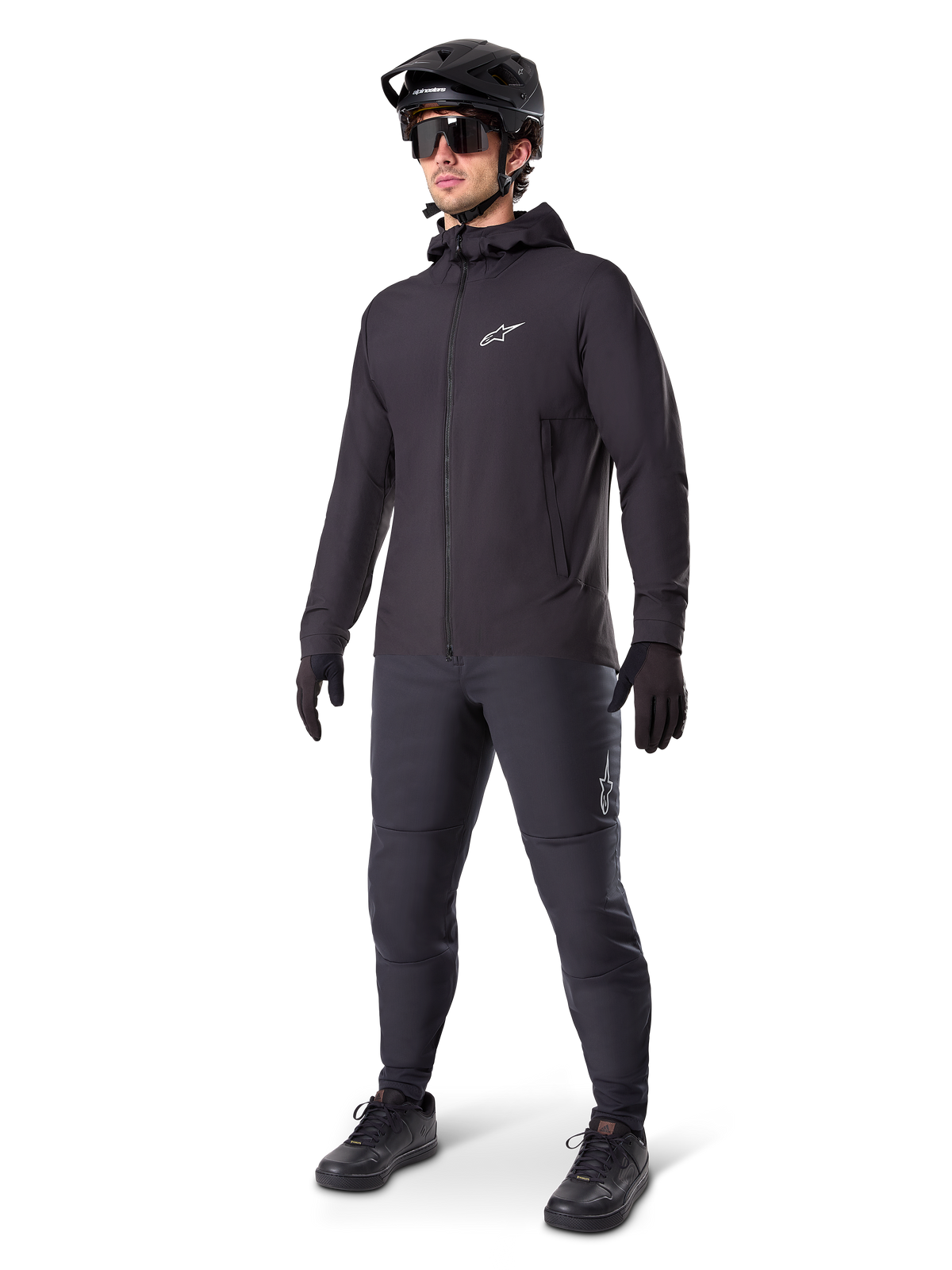 Alpinestars A-Dura Thermal Jacket i svart, bärs av en manlig cyklist med komplett mountainbike-utrustning inklusive svart hjälm, solglasögon och cykelbyxor, lätt isolerad jacka med huva för prestation i kallt väder.