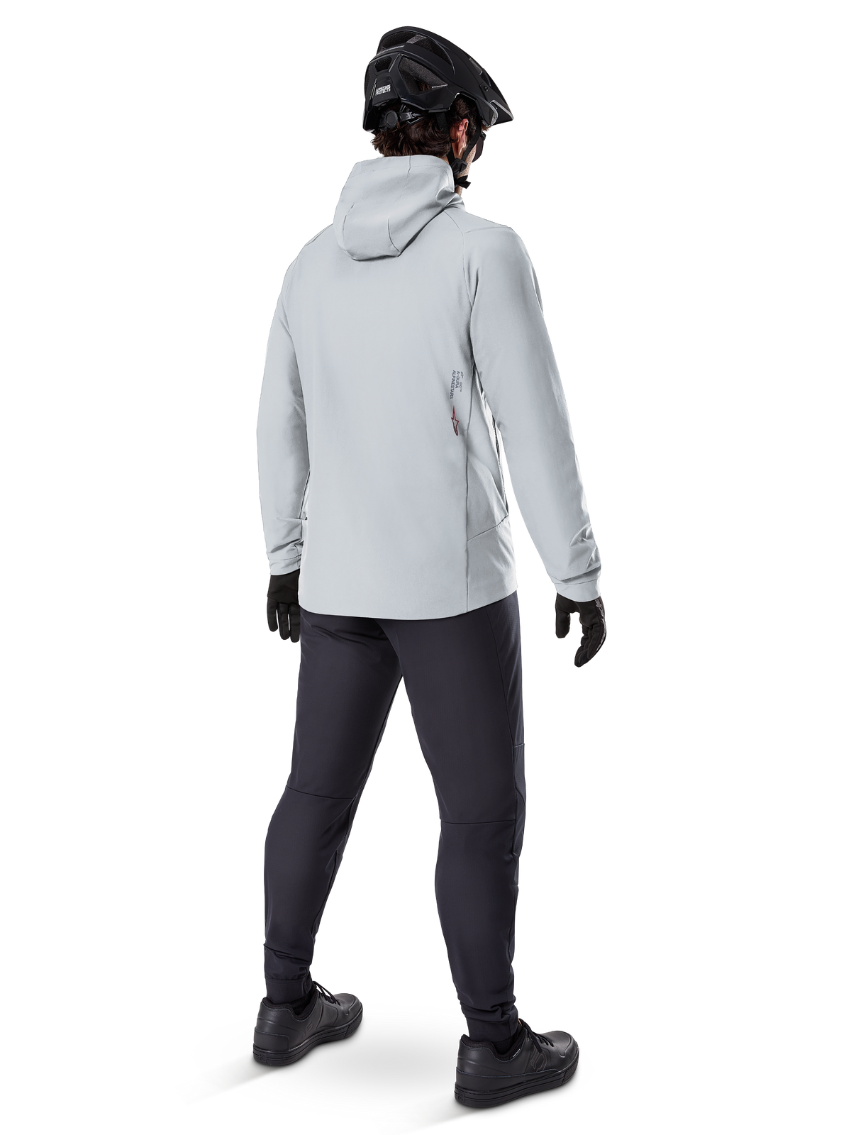 Alpinestars A-Dura Thermal Jacket i Titanium, vy bakifrån av en manlig cyklist i en ljusgrå termojacka med huva, matchad med svart MTB-hjälm, svarta handskar och mörkgrå byxor, funktionell utrustning för mountainbikecykling.