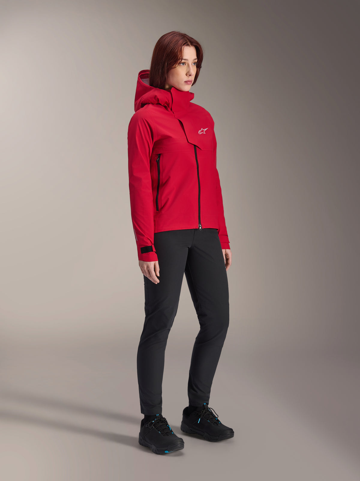 Alpinestars Stella A-Dura Elite Waterproof Jacket för dam, Red Fluo, vattentät MTB-regnjacka med huva och vit Astars-logotyp på bröstfliken, bärs med svarta byxor och svarta mountainbikeskor, teknisk funktionsutrustning för stigcykling
