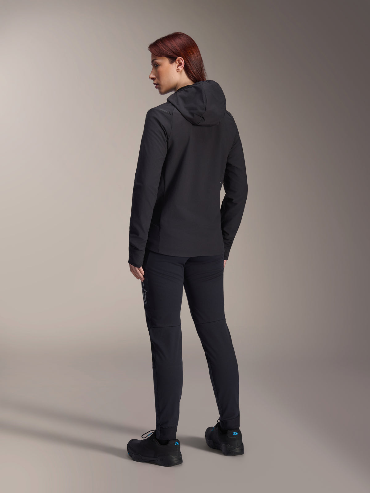 Alpinestars Stella A-Dura Thermal Jacket, Women's MTB cycling jacket, Black, back view highlighting the insulated hood and regular fit, worn with matching black pants and shoes, lightweight thermal insulation for cold-weather riding