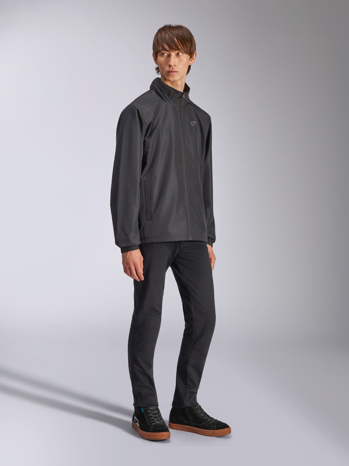 Alpinestars Overhaul Racer Jacket, Black rain shell jacket, worn with black trousers and black sneakers with gum soles, featuring a white star logo on the chest, zip-up front, casual motorsport-inspired sportswear