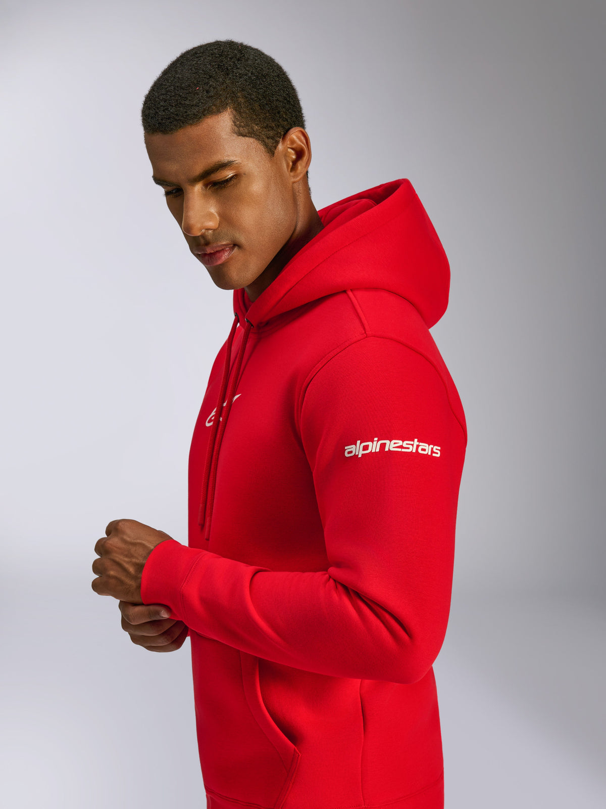 Alpinestars Frontal Hoodie, röd fleece-huvtröja i pullover-modell som bärs av en modell, med vit Alpinestars wordmark-logotyp på ärmen, frontlogotyp, känguruficka och huva med dragsko, avslappnad motorsportinspirerad design