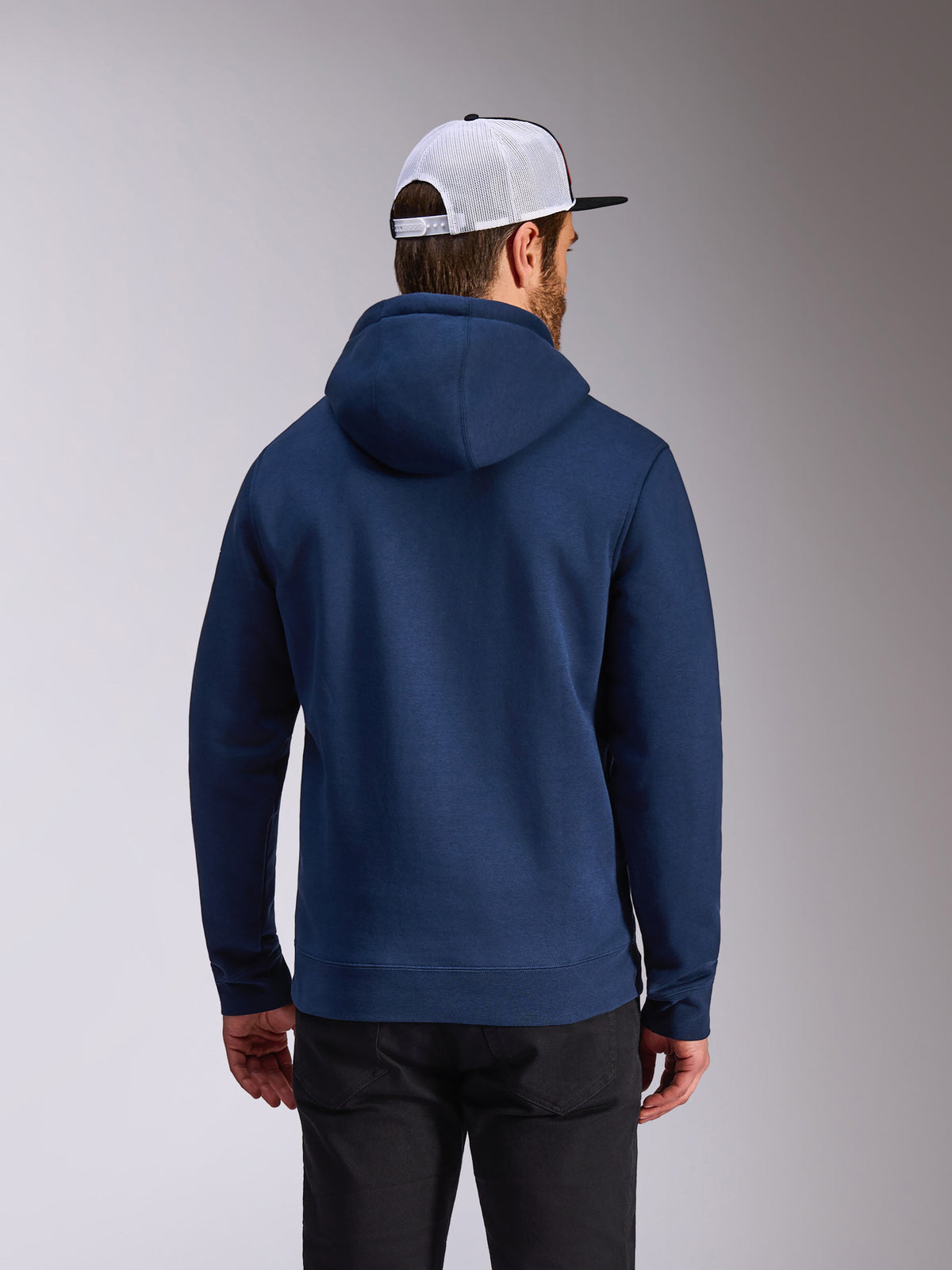Alpinestars Frontal Hoodie, marinblå fleece-huvtröja, baksida av avslappnad streetwear, bärs med svarta byxor och en vit och svart meshkeps, modern motorsport-inspirerad design