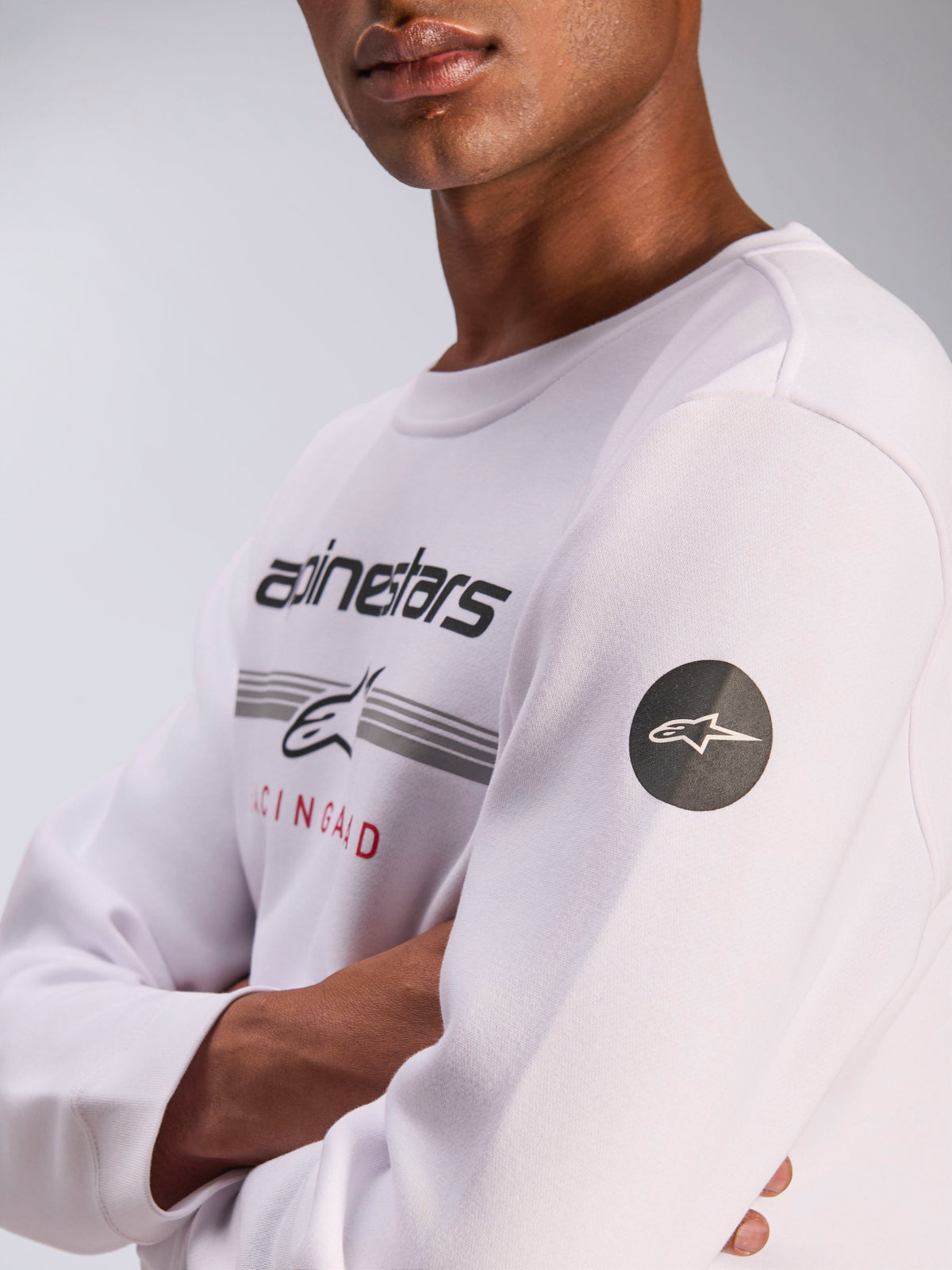 Alpinestars Bettern Crew, white crewneck sweatshirt, casual motorsport streetwear, featuring front chest graphic with Alpinestars wordmark and grey stripes, black circular star logo patch on the sleeve, fleece pullover design