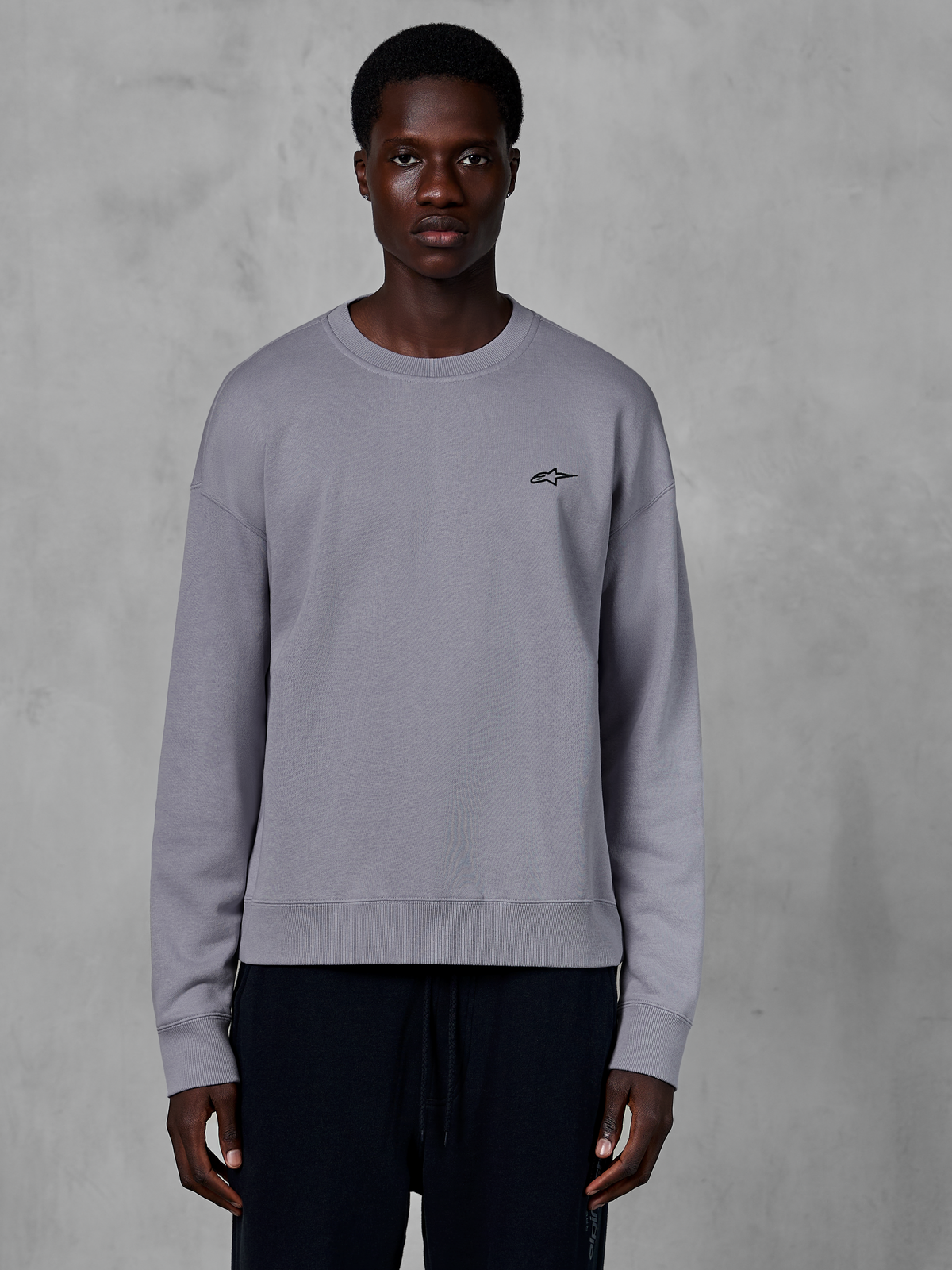 Alpinestars Essentials Ageless Crew, silverfärgad sweatshirt med rund hals bärs av en modell, med en liten svart stjärnlogotyp på bröstet, avslappnad passform med ribbade muddar och fåll, avslappnad motorsport-streetwear