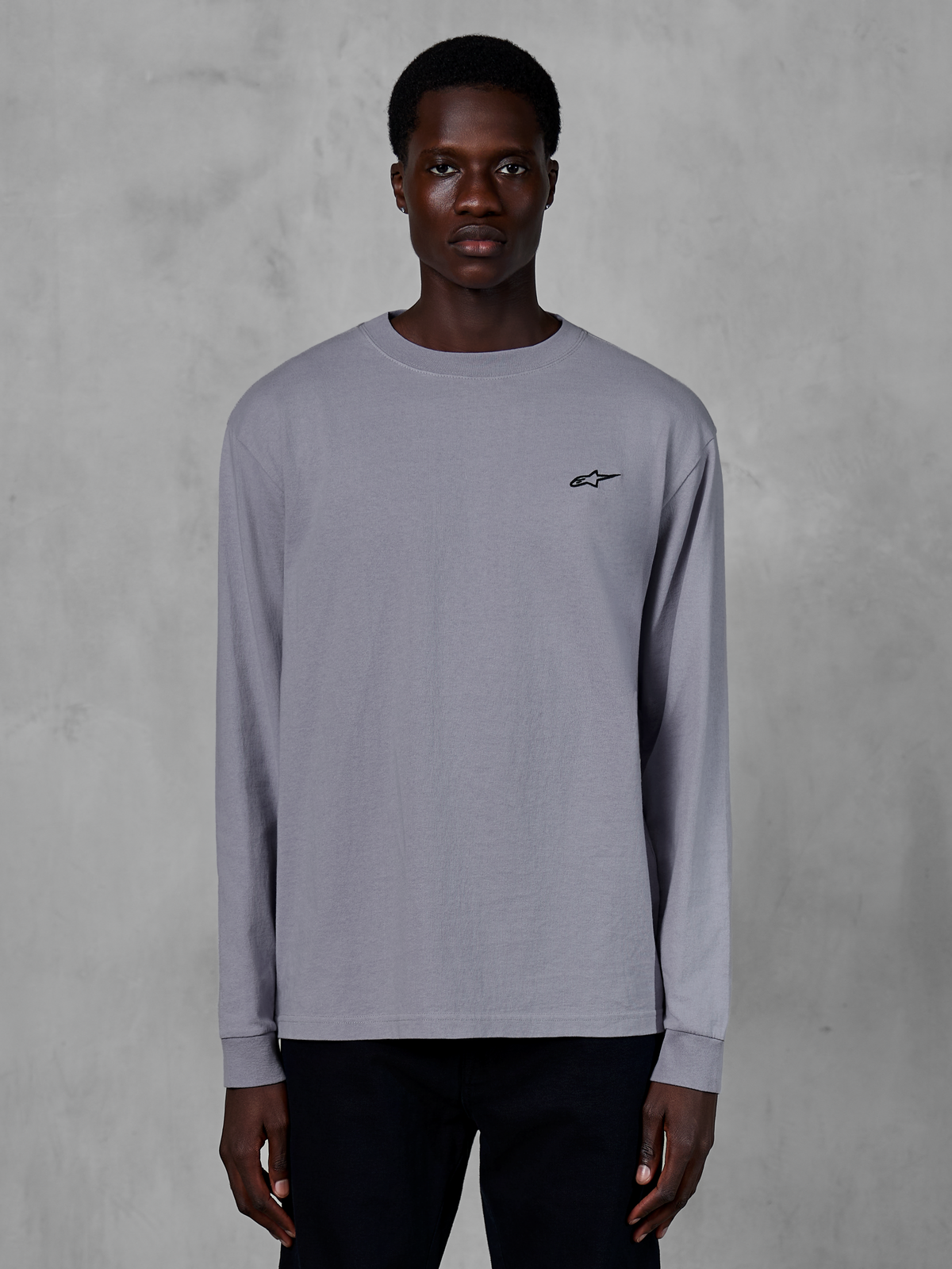 Alpinestars Essentials Ageless LS Tee, långärmad t-shirt, silver, bärs av en modell, med en liten svart Alpinestars-logotyp på bröstet, avslappnad modern passform, streetwear i ekologisk bomull