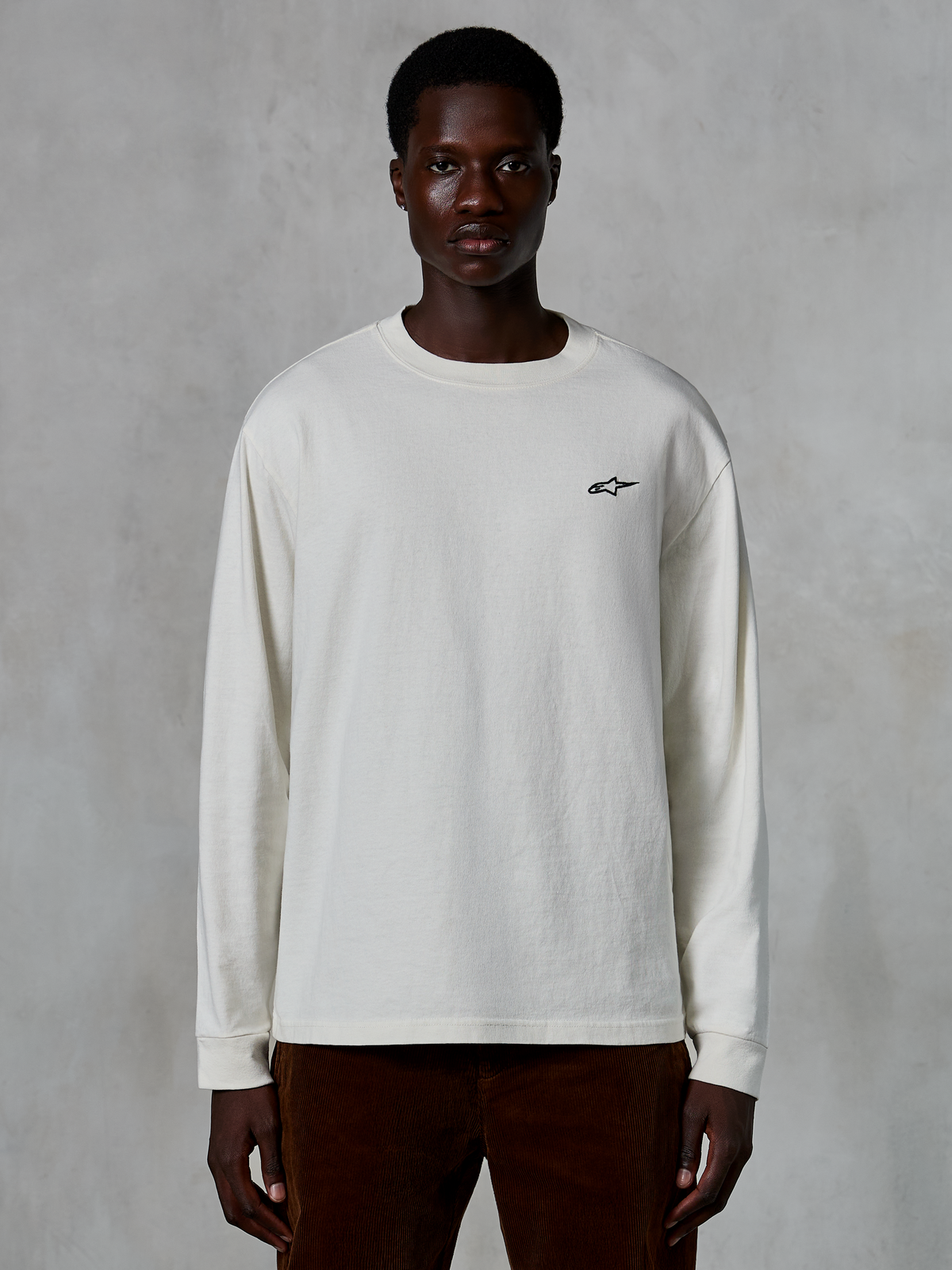 Alpinestars Essentials Ageless LS Tee, långärmad t-shirt, off-white, liten svart stjärnlogotyp på bröstet, avslappnad streetwear, avslappnad passform, bärs av en modell