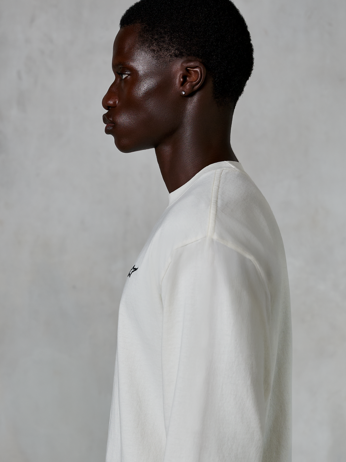 Alpinestars Essentials Ageless LS Tee, långärmad t-shirt, Off White, profilvy av en man i den avslappnade t-shirten, med en liten svart logotyp på bröstet, vardagliga motorsportinspirerade livsstilskläder