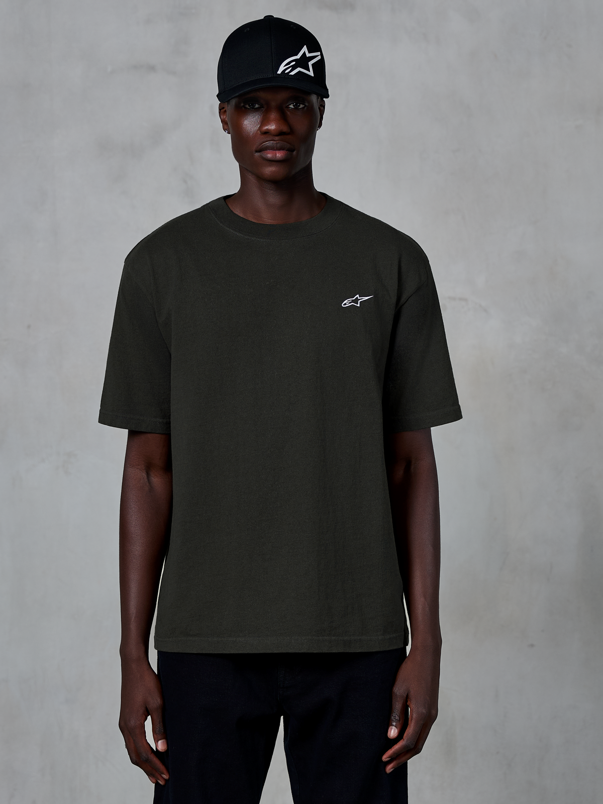 Alpinestars Essentials Ageless SS Tee, kortärmad t-shirt, Off Black, bärs av en modell med en svart keps med logotyp, liten vit Alpinestars-logotyp på bröstet, avslappnad motorsportinspirerad streetwear